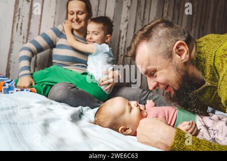 Heureux père embrassant bébé fille et mère assis avec son fils sur le lit à la maison Banque D'Images