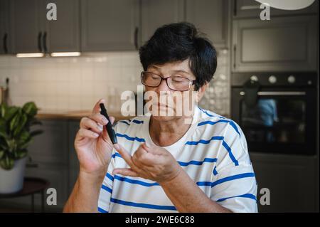 Femme âgée ponçant le doigt pour un test de glycémie Banque D'Images