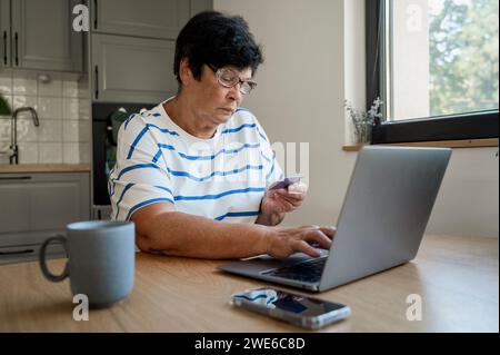 Femme âgée faisant le paiement par carte de crédit par ordinateur portable à la maison Banque D'Images