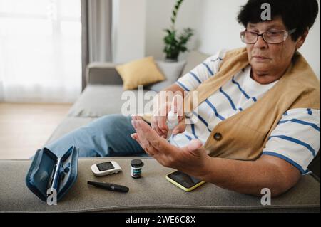 Femme âgée utilisant un désinfectant pour le test de glycémie à la maison Banque D'Images