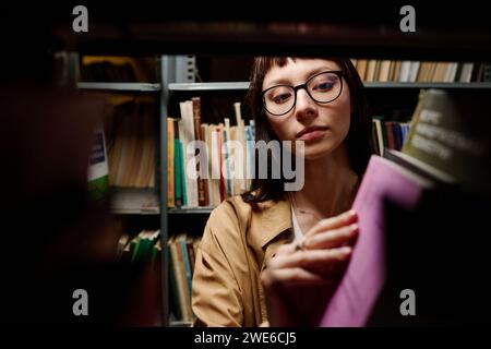 Jeune étudiant à la recherche de livres sur l'étagère dans la bibliothèque Banque D'Images