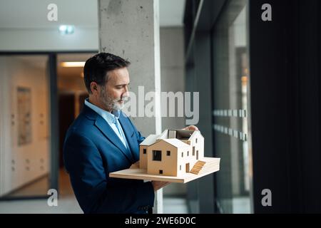 Architecte mature examinant la maison modèle dans le couloir de bureau Banque D'Images