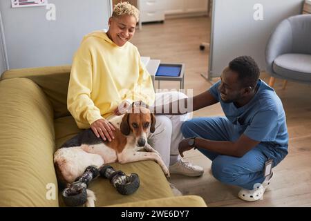 Femme heureuse avec chien vétérinaire caressant sur le canapé dans la clinique Banque D'Images