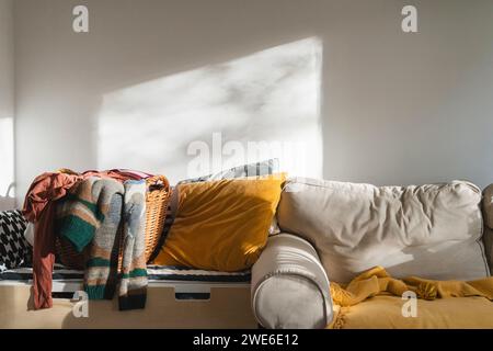 Panier à linge avec des vêtements près du canapé devant le mur blanc Banque D'Images