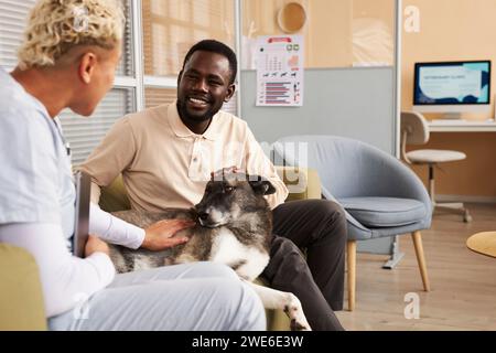 Homme heureux assis avec le chien et parlant au vétérinaire en clinique Banque D'Images