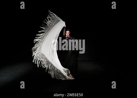 Femme gracieuse exécutant la danse flamenco avec châle sur fond noir Banque D'Images