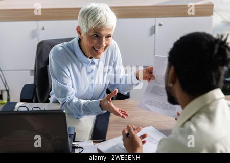 Femme d'affaires souriante discutant de documents avec un collègue au bureau Banque D'Images