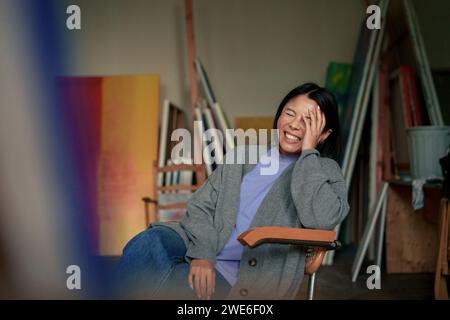 Peintre heureux avec les yeux fermés assis sur la chaise dans l'atelier d'art. Banque D'Images