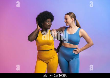 Souriant jeunes amies féminines multiraciales se regardant tout en se tenant debout sur fond coloré Banque D'Images