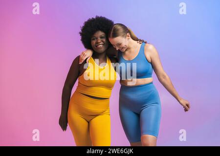 Heureux jeunes amies féminines multiraciales debout avec les bras autour sur fond coloré Banque D'Images