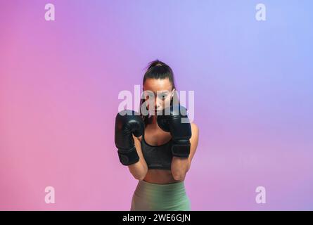 Jeune femme confiante avec des gants de boxe noirs sur fond coloré Banque D'Images