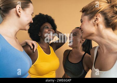 Amies féminines multiraciales joyeuses riant sur fond beige Banque D'Images