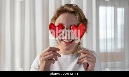 Femme heureuse tenant des biscuits en forme de coeur sur les yeux à la maison Banque D'Images