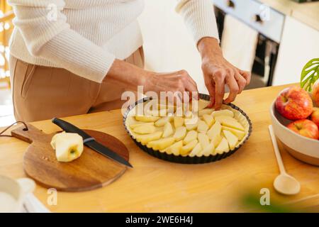 Femme mature arrangeant des morceaux de pomme sur la tarte à la maison Banque D'Images