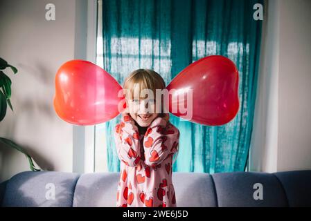 Fille joueuse tenant des ballons sur les oreilles à la maison Banque D'Images