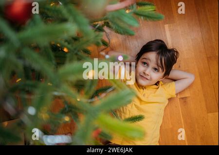 Garçon allongé sur le sol sous l'arbre de Noël à la maison Banque D'Images