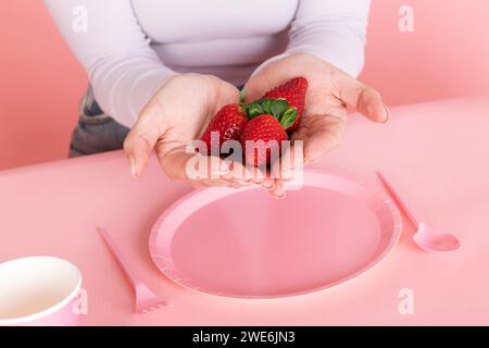 Femme tenant des fraises en main sur une assiette vide rose Banque D'Images