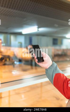 Vue rapprochée d'un homme méconnaissable à l'aide d'un smartphone à la fenêtre d'enregistrement de l'aéroport avec des vêtements décontractés. Les gens qui voyagent avec des styles de vie technologiques. Phon Banque D'Images