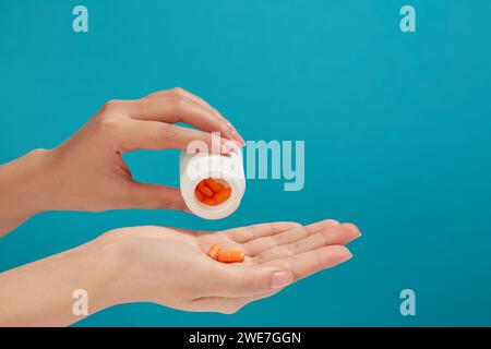 Une boîte à médicaments verse beaucoup de pilules orange dans la main d'une femme. Fond bleu. Différentes pilules prescrites par le médecin Banque D'Images