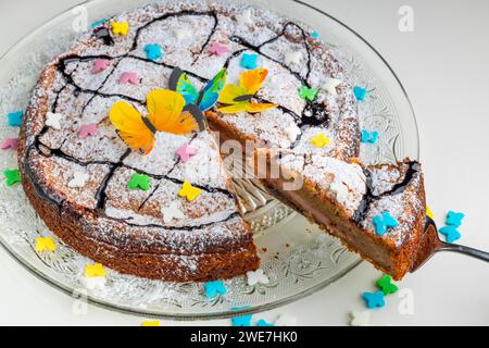 Gâteau succulent avec décoration papillon et saupoudrages colorés sur une assiette en verre, base blanche Banque D'Images