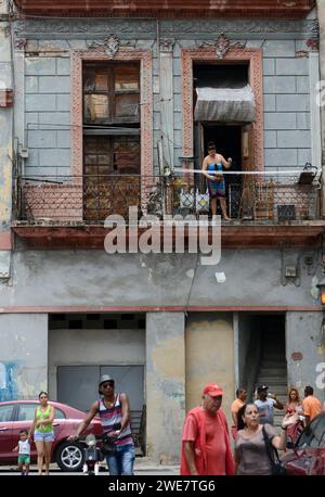 Une femme debout sur le balcon d'un immeuble utilise une corde pour soulever son sac acheté chez un vendeur de rue dans la vieille Havane, à Cuba. Banque D'Images