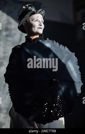 Portrait dramatique à faible angle de l'interprète de mime féminin agissant sur scène sous les projecteurs et tenant un parapluie Banque D'Images