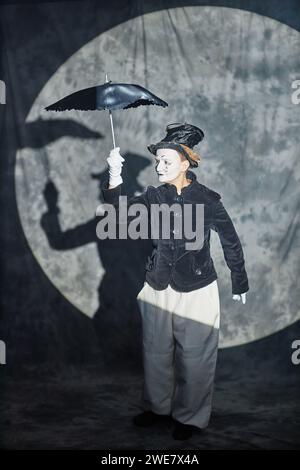 Portrait vertical pleine longueur de l'interprète de mime classique agissant sur scène sous les projecteurs et tenant un parapluie Banque D'Images