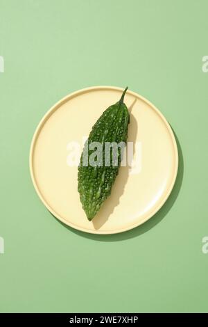 Melon amer vert frais bio mis sur un plat rond jaune. Le melon amer (Momordica charantia) peut vous aider à réduire le taux de cholestérol sanguin Banque D'Images