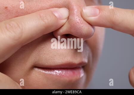 Femme popping bouton sur son nez sur fond gris, closeup Banque D'Images