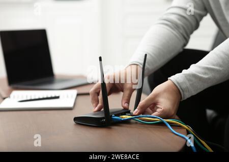 Homme insérant le câble dans le routeur Wi-Fi à la table en bois à l'intérieur, gros plan Banque D'Images