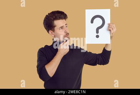 L'homme pensif regarde un morceau de papier avec un point d'interrogation dessiné dessus, qu'il tient en main Banque D'Images