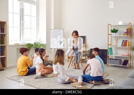 Groupe d'élèves de l'école primaire assis sur le sol écoutant l'enseignant en classe Banque D'Images