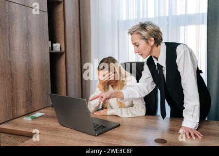 Agressive femme d'âge moyen patron grondant une employée pour mauvais résultat sur le lieu de travail. Cadre insatisfait pointant du doigt la réprimande des ordinateurs portables Banque D'Images