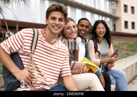 Des personnes diverses souriant assis dehors tenant des dossiers. Groupe multiculturel d'étudiants heureux regardant la caméra avec des sacs à dos et des cahiers. Banque D'Images