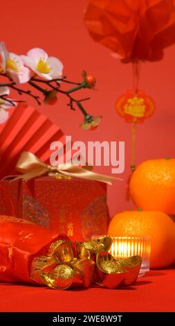 Fond du nouvel an lunaire chinois, thème rouge. or dans un sac en soie, boîte cadeau rouge avec noeud doré, éventail de papier, oranges, branche de fleur de prunier, bougie Banque D'Images