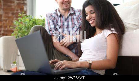 Une fille souriante assise sur le sol avec un ordinateur portable près d'un gars Banque D'Images