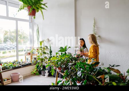 Femme asiatique fleuriste porte tablier parlant et présenté au client et vendant des plantes tout en travaillant dans le magasin d'usine. Petite entreprise et démarrage Banque D'Images