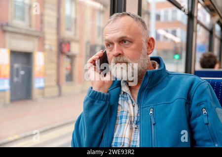 un homme barbu dans une veste bleue parlant au téléphone dans un bus. Concept de style de vie Banque D'Images