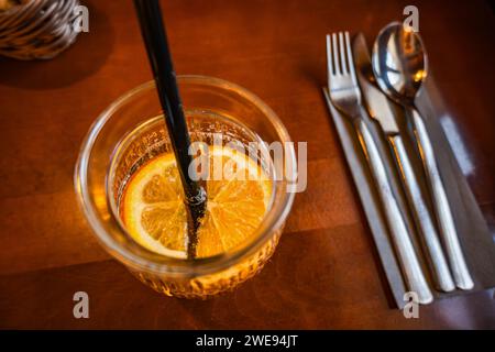 Boisson fruitée avec des tranches d'orange en verre avec de la paille, des couverts. Gros plan sur la table du restaurant, vue de dessus. Banque D'Images