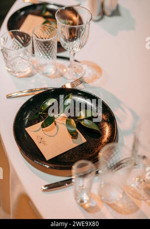 Table de table lors d'un mariage de luxe. Table de fête. Décoration classique, verres, assiettes sombres et carte de place pour les clients Banque D'Images