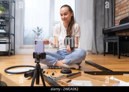 La jeune fille est confuse et consulte par lien vidéo en essayant d'assembler des meubles. Banque D'Images