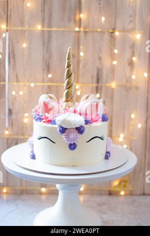 Gâteau licorne avec corne fondante dorée, cils et glaçage au fromage à la crème sur fond de bokeh festif Banque D'Images