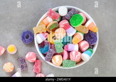 Bol de bonbons de gelée mélangés sur la surface grise tachetée. Pose à plat avec espace de copie Banque D'Images