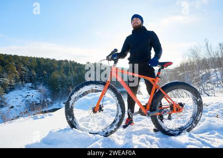 Jeune cycliste barbu positif tenant fatbike et debout sur la montagne réfléchissant à la vie Banque D'Images