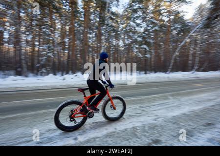 Vue latérale grand angle de cycliste roulant pro vélo sur la route dans la forêt d'hiver, espace de copie Banque D'Images