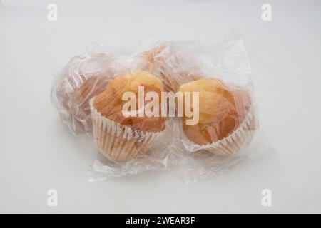 Gros plan de quelques muffins industriels enveloppés dans du plastique transparent isolé sur fond blanc Banque D'Images