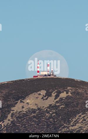 Madrid, Espagne. 24 janvier 2024. Une lune presque pleine de janvier (connue sous le nom de Wolf Moon) se lève au-dessus du centre de télédiffusion espagnol de Bola del Mundo, inauguré en 1959, situé à Navacerrada, à 2 262 mètres de haut. Crédit : Marcos del Mazo/Alamy Live News Banque D'Images