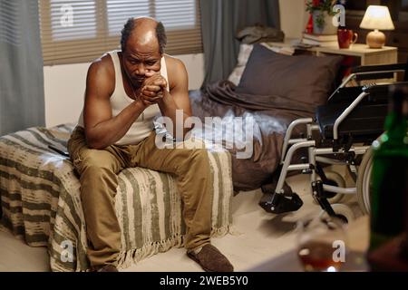 Homme afro-américain avec handicap physique assis sur son lit seul souffrant de solitude Banque D'Images