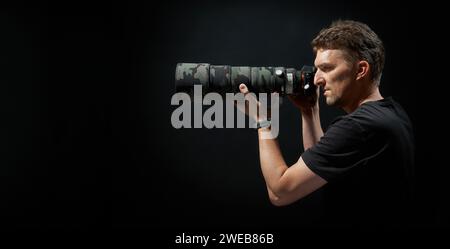 jeune photographie visant avec appareil photo et grand objectif avec couvercle d'objectif attaché avec motif de style camouflage Banque D'Images