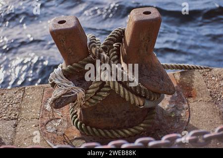 Une Bollard rouillé Double Bitt, enveloppé dans des lignes d'amarrage (cordes) et une chaîne, à la lumière du soleil. Côté quai, Canary Wharf, Londres Banque D'Images